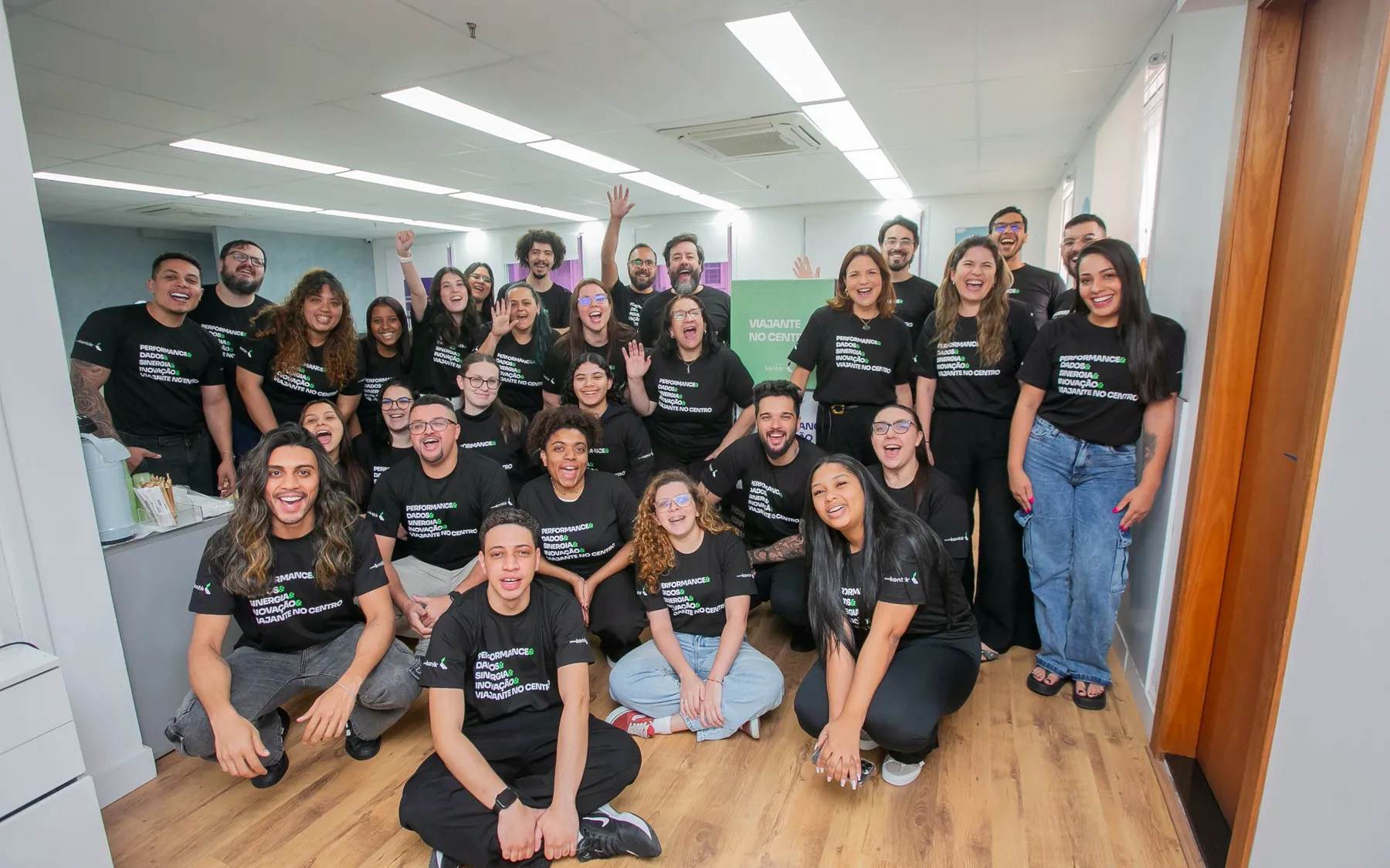 Time da Kontrip reunido no escritório, sorrindo e acenando, com camisetas da campanha de cultura